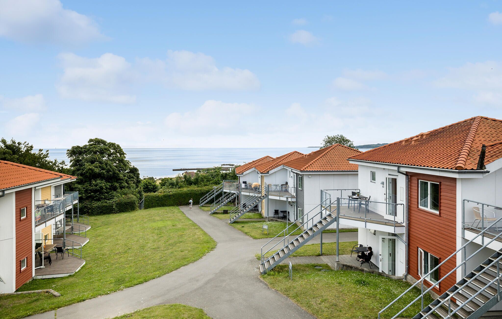 A row of modern seaside cottages with outdoor seating, a central pathway, and a view of the sea.