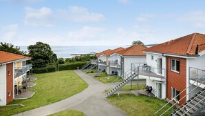 Une rangée de maisons de vacances modernes, situées en bord de mer, dotées d’espaces extérieurs aménagés, d’un chemin central et offrant une vue sur la mer.