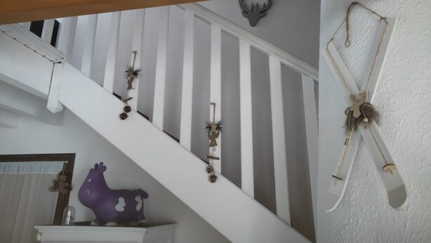Una escalera con barandas blancas, una cabeza de venado decorativa en la pared y una figura de llama morada sobre un mueble blanco.