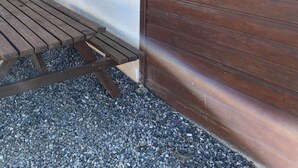 Una terraza de madera con un sendero de grava, un portón metálico y una maceta con flores rojas.