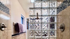 A bathroom with a tiled floor, a shower area with a glass partition, and a towel rack with a purple towel. - Serene Escape in West Sedona w/ Gorgeous Views (Sedona)