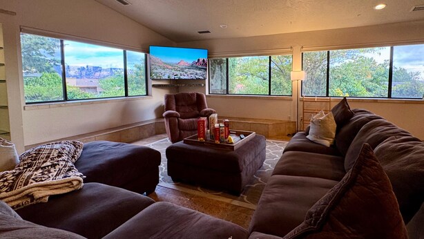A living room with a large window, a flat-screen TV, a brown leather armchair, a brown sofa, and a coffee table with books and a remote control. - Serene Escape in West Sedona w/ Gorgeous Views (Sedona)