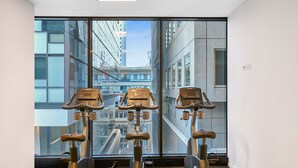 Three stationary bikes in a room with large windows overlooking a cityscape. - Melbourne CBD Stay - Balcony, Gym & Prime City Location (Melbourne)