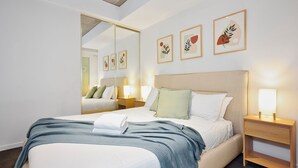 A hotel room with a bed, bedside tables, a mirror, and framed artwork on the wall. - Melbourne CBD Stay - Balcony, Gym & Prime City Location (Melbourne)