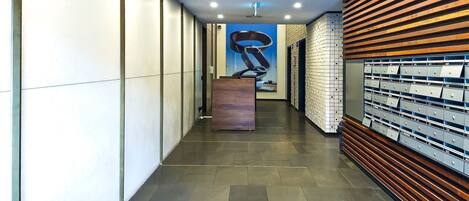 Un pasillo moderno con un panel de listones de madera, una gran escultura azul y una pared de cajas de almacenamiento numeradas.