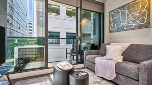 A modern living room with a grey sofa, a glass door leading to an outdoor area, and a contemporary art piece on the wall. - Melbourne CBD Stay - Balcony, Gym & Prime City Location (Melbourne)