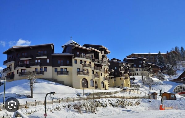 A multi-story hotel with balconies, situated on a snowy slope with clear skies.
