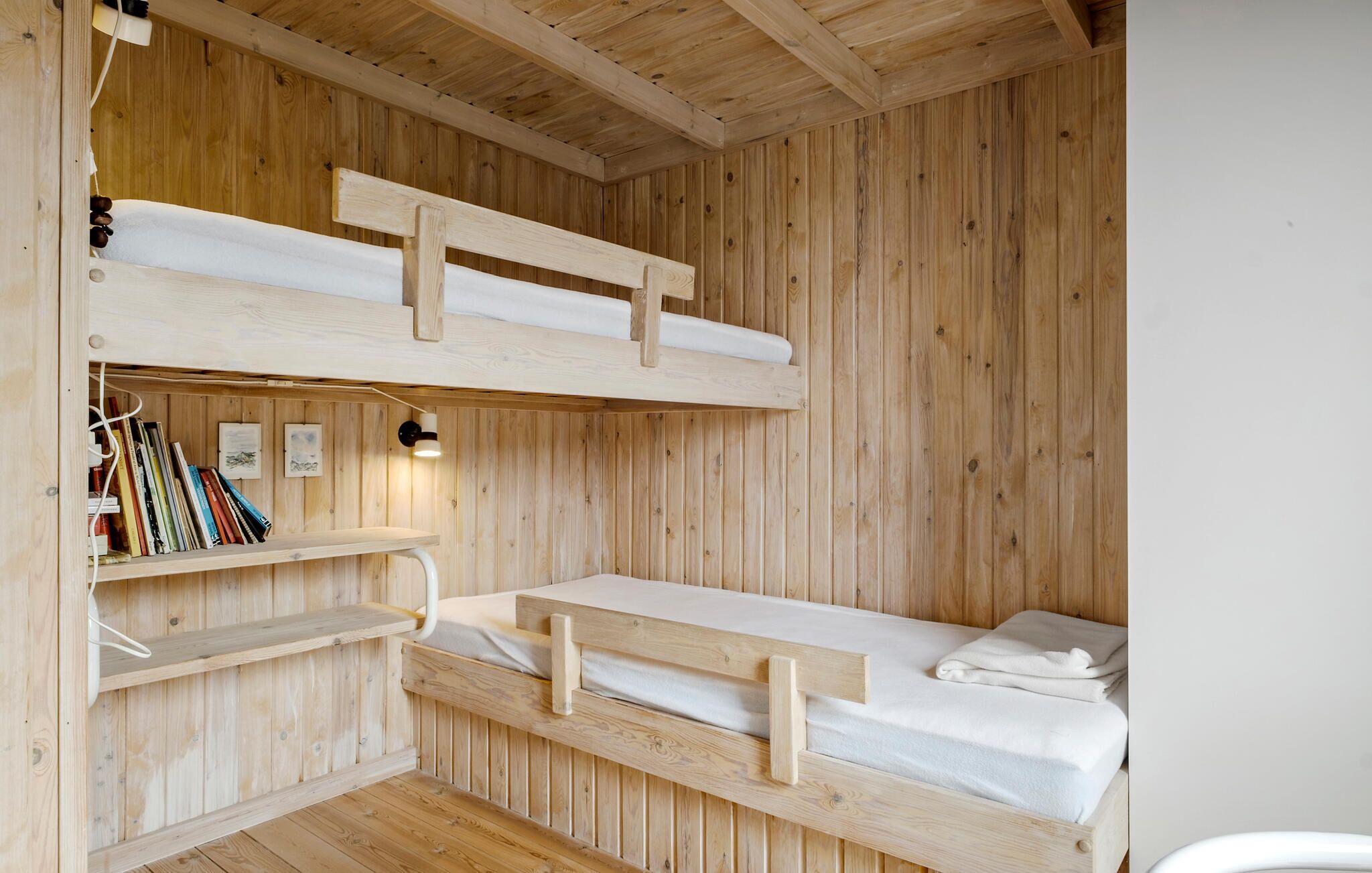 Een kamer met een houten stapelbed, een plank en een bureau, met boeken en een lamp.