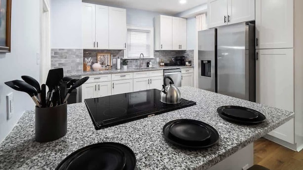 Une cuisine moderne avec des meubles blancs, un plan de travail en granit, un réfrigérateur en acier inoxydable et une plaque de cuisson à induction noire.