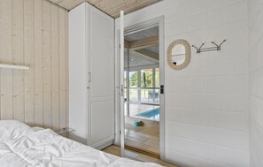 Et soveværelse med en seng, et hvidt klædeskab og en dør, der fører ud til en balkon med udsigt over en swimmingpool.