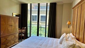 Une chambre à coucher avec un grand lit, une armoire en bois, un bureau avec une chaise et une fenêtre avec des rideaux.