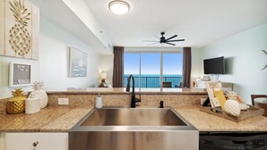 A modern kitchen with a large stainless steel sink, granite countertops, a ceiling fan, and a view of the ocean through large windows.