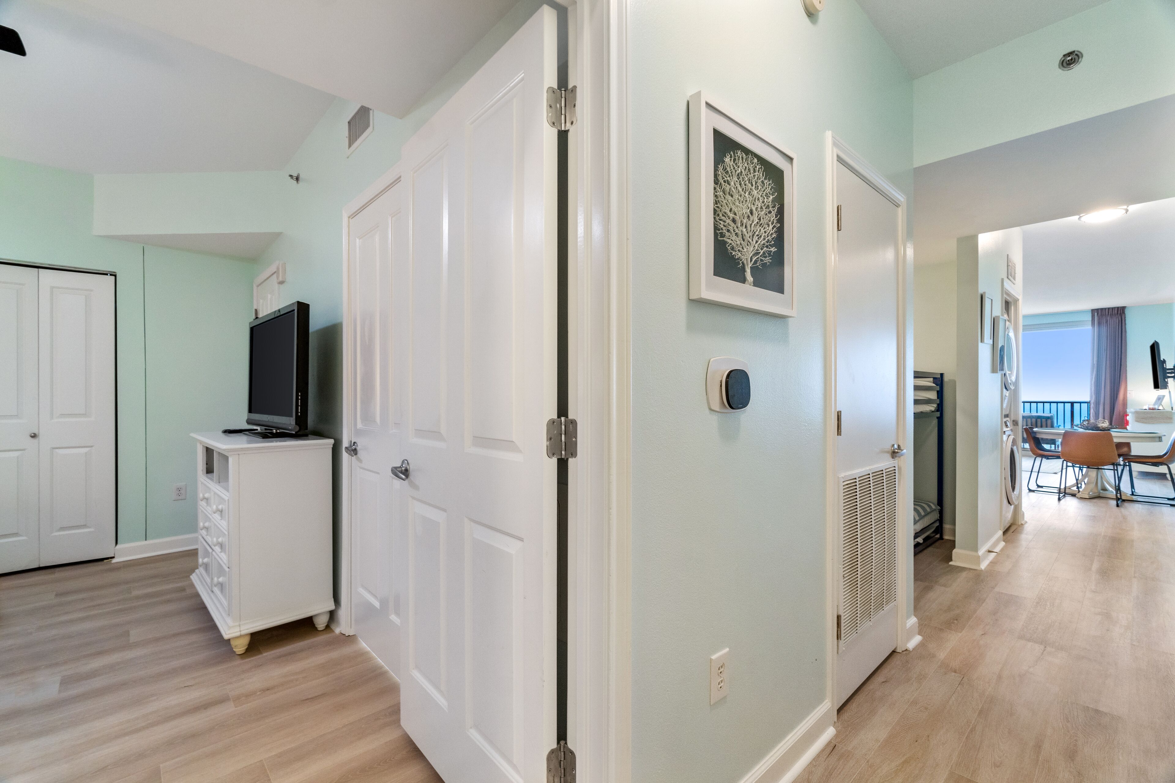A spacious living area with a television on a white cabinet, a dining area with a table and chairs, and a hallway leading to another room.