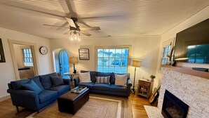 A living room with a blue sofa, a coffee table, a fireplace, and a ceiling fan. - Peaceful, Updated Cottage. Walk to Town & Beach. (Pacific Grove)