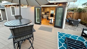 A patio with a round table and chairs, a covered umbrella, and a view into the house. - Peaceful, Updated Cottage. Walk to Town & Beach. (Pacific Grove)