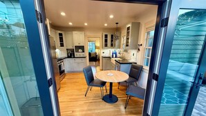 A modern kitchen with white cabinets, a central island, and a dining area with a round table and chairs. - Peaceful, Updated Cottage. Walk to Town & Beach. (Pacific Grove)