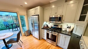 A modern kitchen with stainless steel appliances, white cabinetry, and a wooden floor. - Peaceful, Updated Cottage. Walk to Town & Beach. (Pacific Grove)