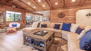 A cozy log cabin interior with a large sofa, a coffee table, and a stone fireplace. - Buffalo Lodge|Hot Tub, EV Charge, Gated, By Slopes (Big Bear)