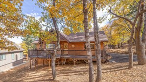 A log cabin with a deck and a covered porch, surrounded by trees with autumn foliage. - Buffalo Lodge|Hot Tub, EV Charge, Gated, By Slopes (Big Bear)