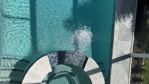Uma banheira de hidromassagem circular com borda em azulejo, rodeada por uma piscina com água cristalina.