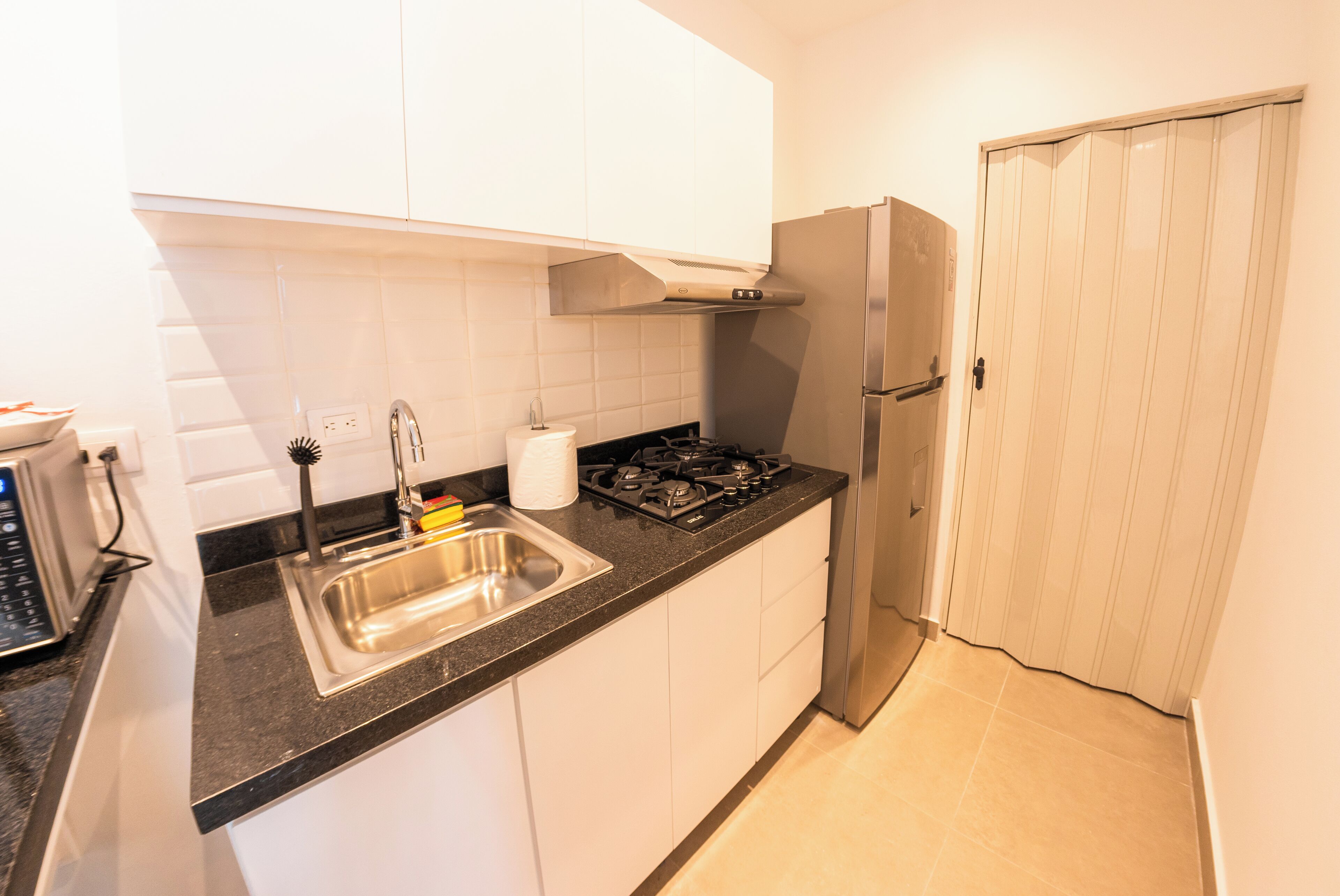 A compact kitchen with white cabinets, a stainless steel sink, a gas stove, and a refrigerator.