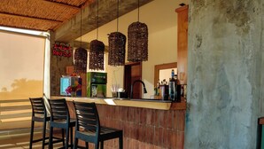 A bar area with a concrete wall, hanging wicker light fixtures, and a logo on the wall. - Las Golondrinas Cabarete (Cabarete)