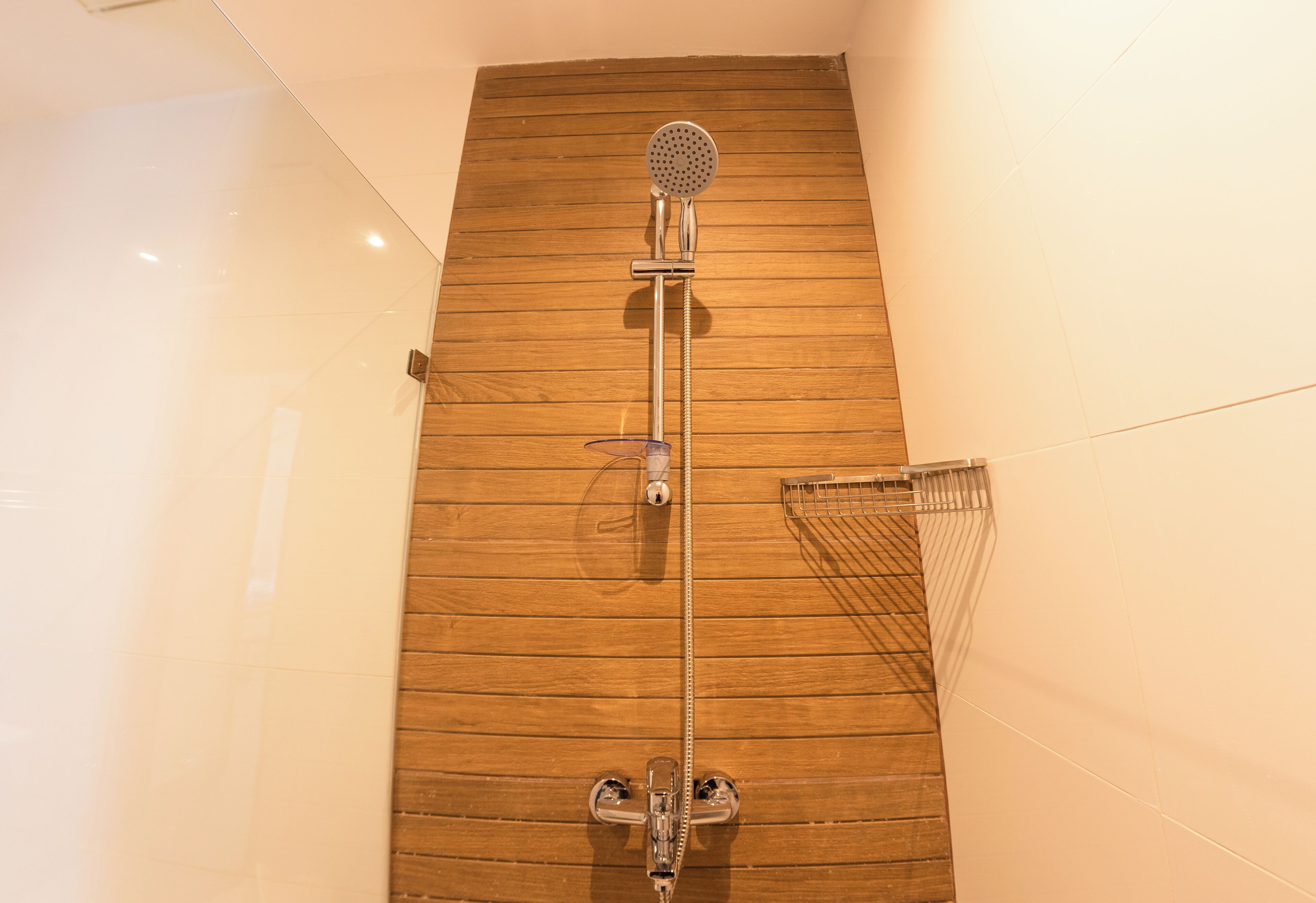 A shower with a wooden panel wall, a handheld showerhead, and a wall-mounted towel rack.