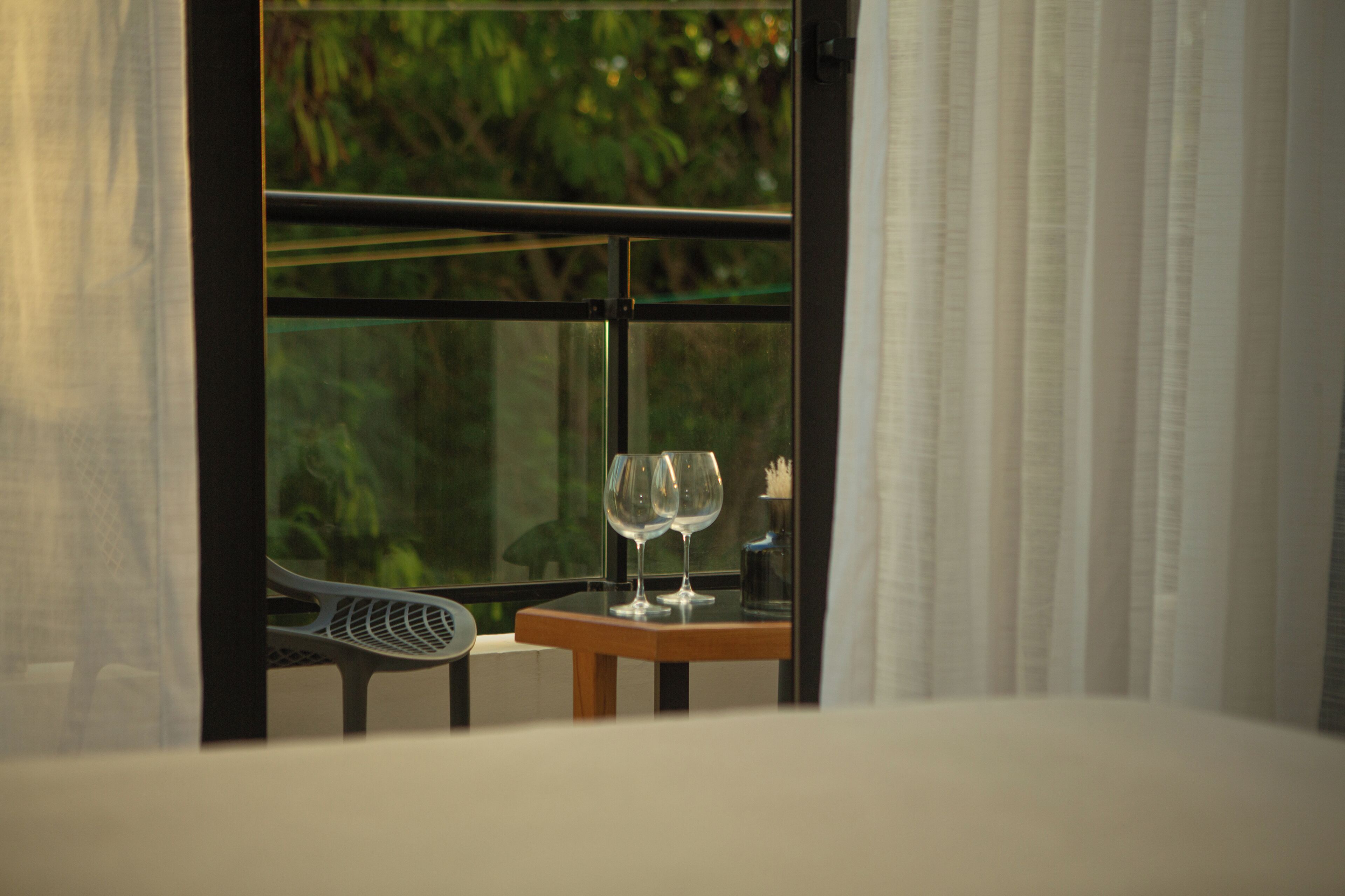 Une chambre avec un lit, une fenêtre avec des rideaux et une petite table sur laquelle sont posés deux verres à vin.