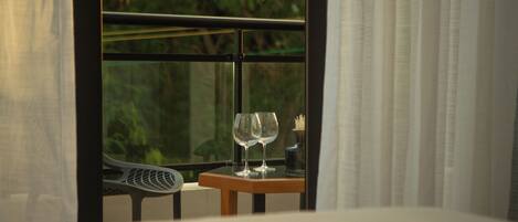 A room with a bed, a window with curtains, and a small table with two wine glasses.