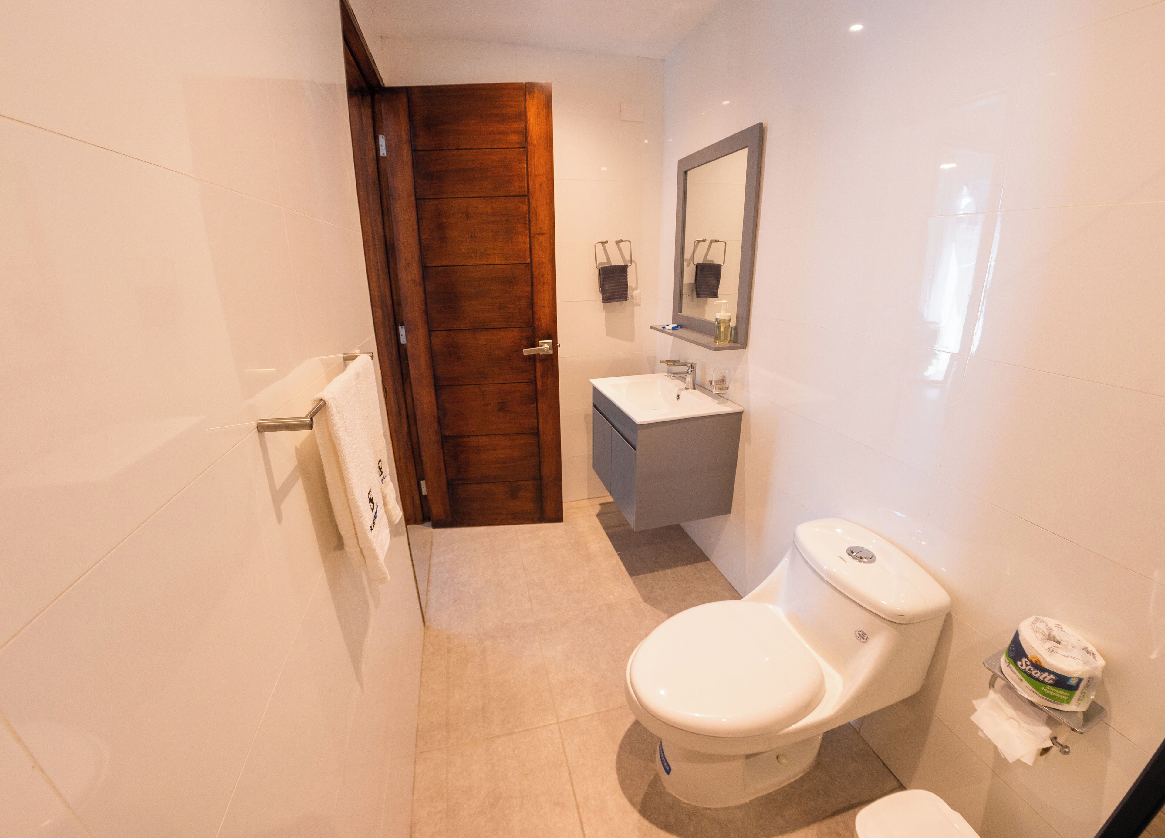 Un baño moderno con puerta de madera, lavamanos blanco y un inodoro.