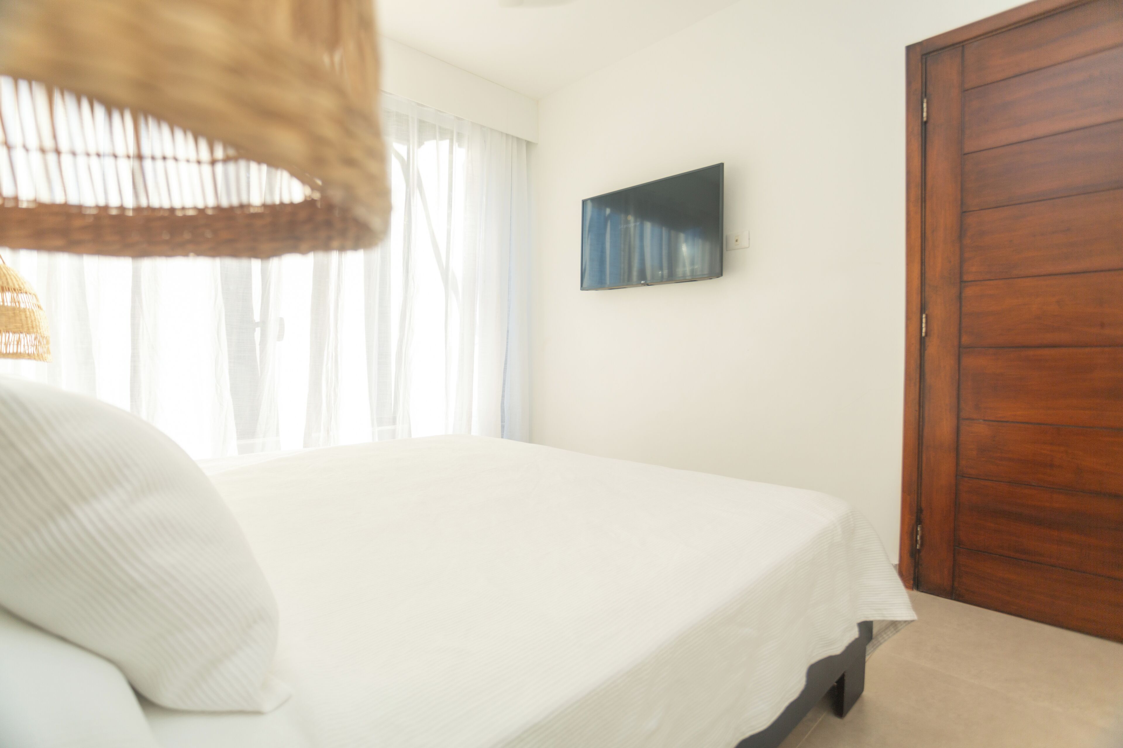 Ein Schlafzimmer mit einem Bett, einem an der Wand montierten Fernseher und einer Holztür.