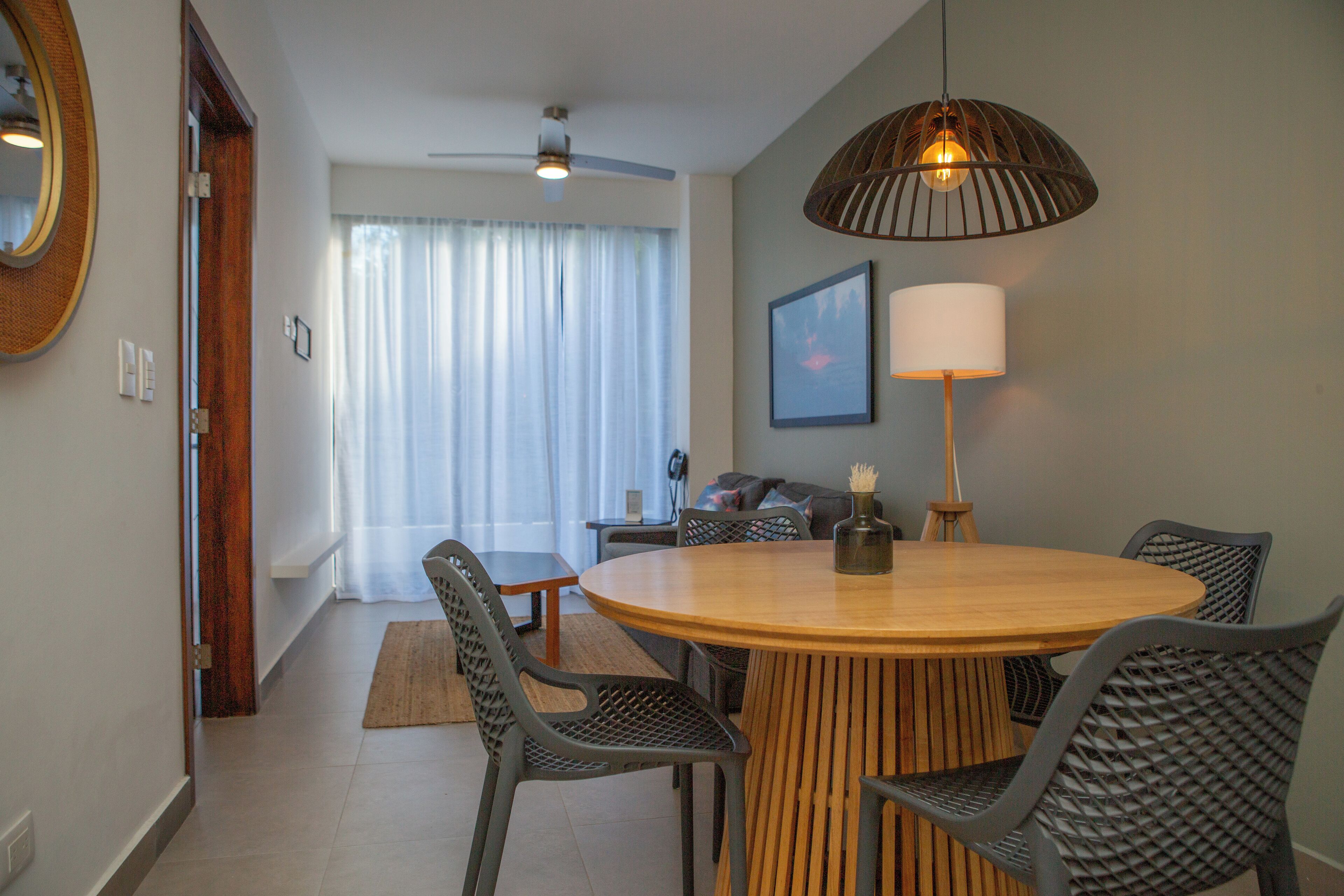 Un comedor con una mesa redonda de madera, cuatro sillas, un ventilador de techo y una lámpara colgante.