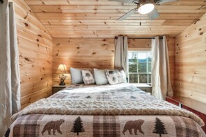 A wooden cabin bedroom with a bed, a window, and a ceiling fan. - Amazing Location - Secluded/Private - Cozy 2-bedroom Log Cabin - Hot Tub (Sevierville)