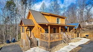 Une cabane en rondins dotée d’une véranda, d’un escalier et d’un panneau solaire sur le toit.