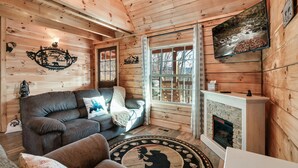 L’intérieur chaleureux d’un chalet, avec un décor en bois, une cheminée, un canapé et un téléviseur fixé au mur.