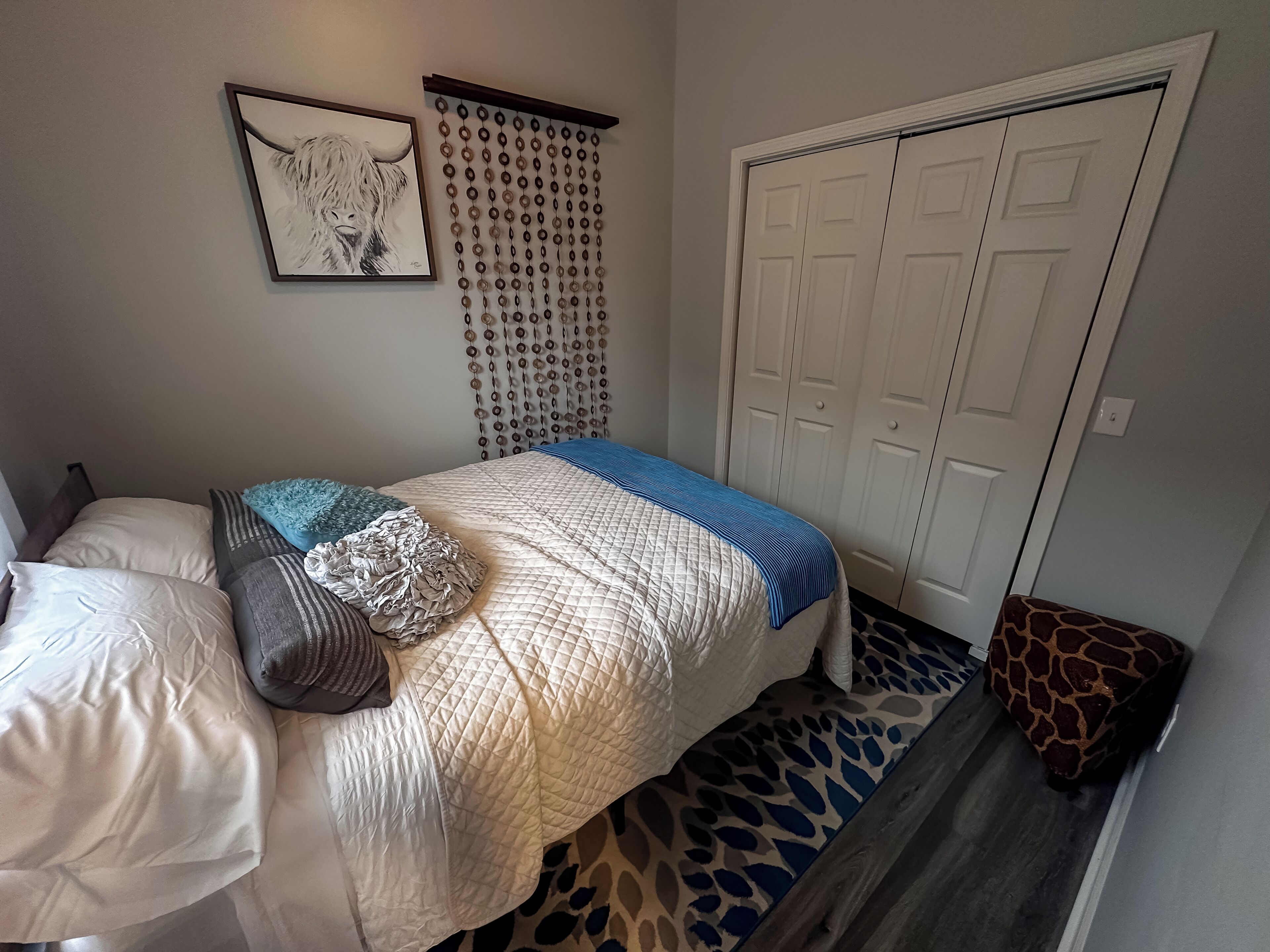 A bedroom with a bed, a wardrobe, a door, and a wall with a hanging decoration.