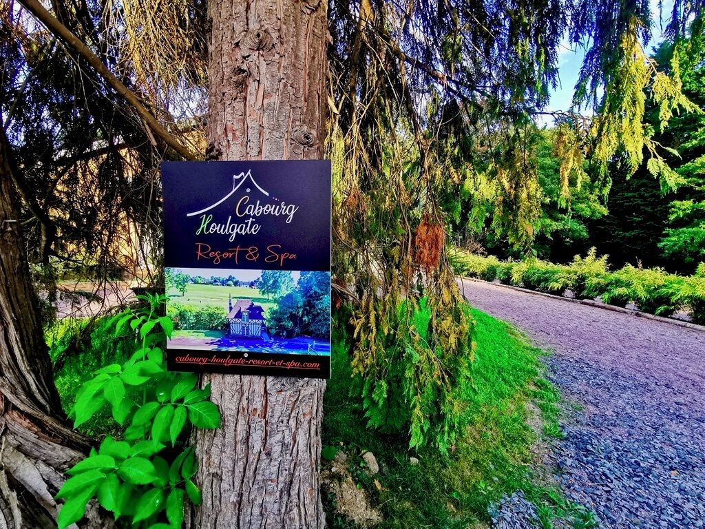 Schild für Caburgate Resort & Spa an einem Baum, mit Blick auf eine Straße und Grün im Hintergrund.
