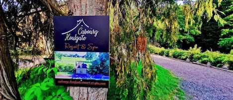Schild für Caburgate Resort & Spa an einem Baum, mit Blick auf eine Straße und Grün im Hintergrund.