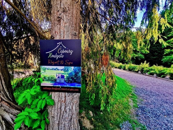 A sign for Caburgate Resort & Spa attached to a tree, with a view of a road and greenery in the background.
