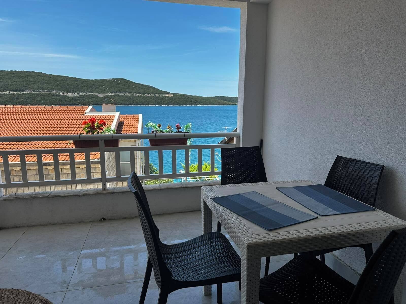 A balcony with a table and chairs, overlooking a body of water and buildings.