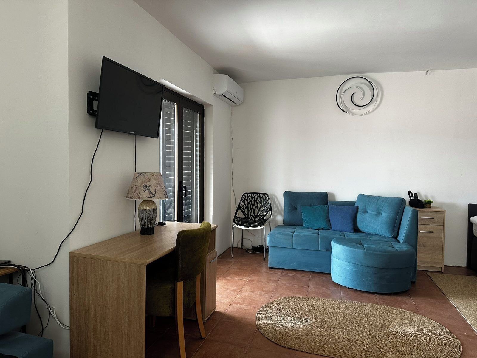Un saló modern amb un escriptori de fusta, un sofà blau, un televisor fixat a la paret i una decoració espiral a la paret.