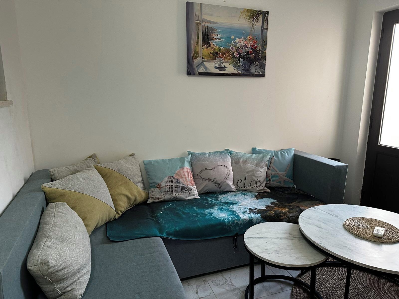 A modern living room with a sectional sofa, a round coffee table, and a painting of a coastal scene.