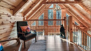 A wooden cabin interior with a high ceiling, a bench with a cushion, a bear statue, and a staircase leading to an upper level. - Log Cabin Amazing Location - Private - Cozy 3-bedroom Sleeps 8 - Hot Tub (Sevierville)