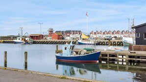 Un puerto con barcos amarrados, un faro y casas rojas al fondo.