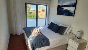 Une chambre avec un grand lit, une table de chevet, une fenêtre avec des rideaux et un tableau au mur.