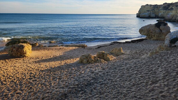 Une plage avec une eau d’un bleu limpide, un rivage sablonneux et des formations rocheuses.