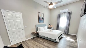 A bedroom with a bed, a desk, a chair, a ceiling fan, and a window with curtains.