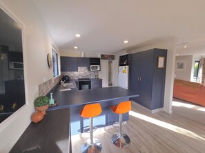 A modern kitchen with a central island, bar stools, and a microwave.