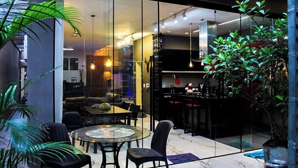 A modern interior with a glass dining area, black furniture, and a large potted plant. - Morumbi Triplex House with Jacuzzi (São Paulo)
