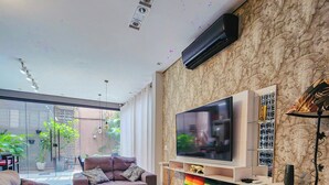 A modern living room with a large flat-screen TV, comfortable seating, a patterned rug, and a stone wall. - Morumbi Triplex House with Jacuzzi (São Paulo)